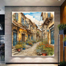 Вчитај ја сликата во галериски мод за гледање, Сликовита калдрмисана уличка со стари камени куќи, сини прозорци, улични фенери и цветни саксии под ведро небо.